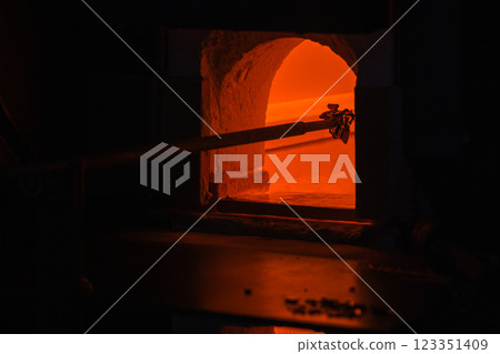Molten glass on a blowpipe is inside of an open furnace, glass blowing Molten glass on a blowpipe is inside of an open furnace, glass blowing 123351409