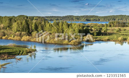 Tranquil scenic view of a calm river bordering vibrant green foliage 123351565
