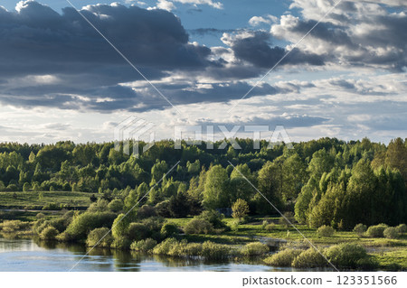 Lush green trees line a river under a dramatic cloudy sky 123351566