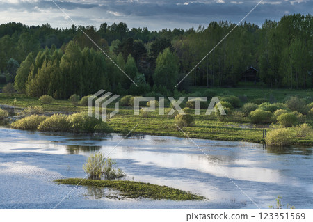 A serene floodplain with vibrant green trees and shrubs framing 123351569