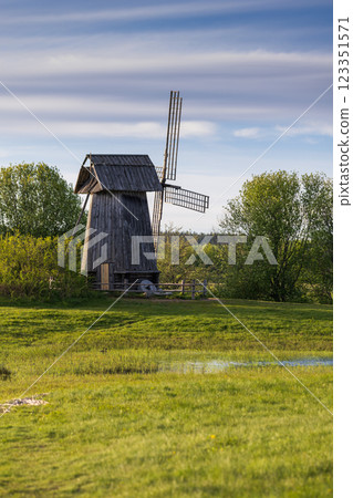 Old wooden windmill surrounded by green grass, trees, vertical photo 123351571