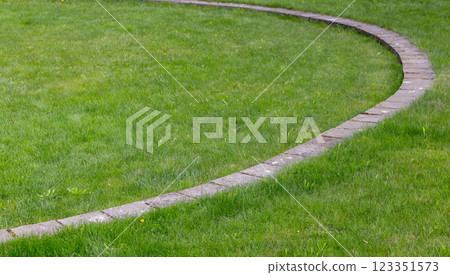 A well-maintained brick pathway curves through a vibrant green lawn 123351573