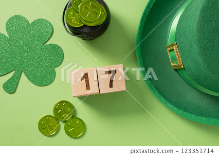 St Patrick's Day and 17 March concept with date on wooden blocks, traditional decoration shamrock, clover leaves and green coins on light green background. View from above. Festive invitation. 123351714