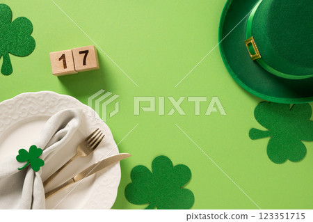 St Patrick's Day and 17 March frame with white plate and traditional decoration, shamrock, clover leaves and green coins on light green background. View from above. Festive invitation. 123351715