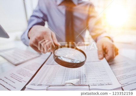 Businessman looking through a magnifying glass to documents Businessman looking through a magnifying glass to documents 123352159