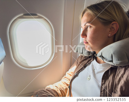 Passenger woman is flying in plane. Girl sitting in airplane looking out window going on trip vacation travel. Traveling female inside plane enjoying flight. Traveling girl 123352535