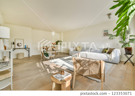 A stylish modern living room featuring a cozy sofa, light wooden flooring, and lush indoor plants, creating a warm and inviting atmosphere. 123353071