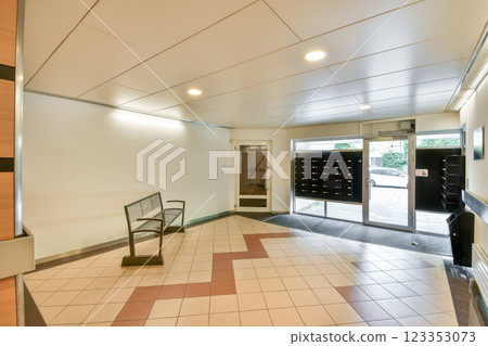 A contemporary indoor lobby featuring sleek design elements, including a patterned floor and a bench, complemented by mailboxes for residents. A contemporary indoor lobby featuring sleek design elements, including a patterned floor and a bench, complemented by mailboxes for residents. 123353073