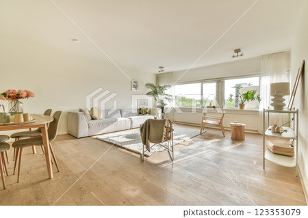 A beautifully designed modern living room featuring a cozy sofa, dining table, and large windows that bring natural light, creating an inviting atmosphere. 123353079