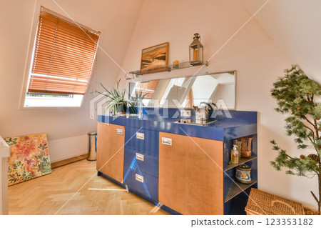 A well-lit modern kitchen featuring wooden cabinets, a vibrant painting, and potted plants adding a fresh touch to the space. A well-lit modern kitchen featuring wooden cabinets, a vibrant painting, and potted plants adding a fresh touch to the space. 123353182