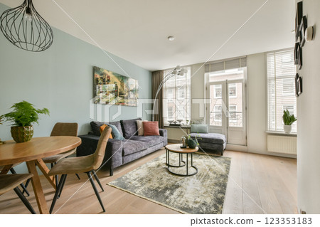 A stylish modern living room featuring comfortable furniture, greenery, and ample natural light. The decor blends contemporary design with inviting aesthetics. 123353183