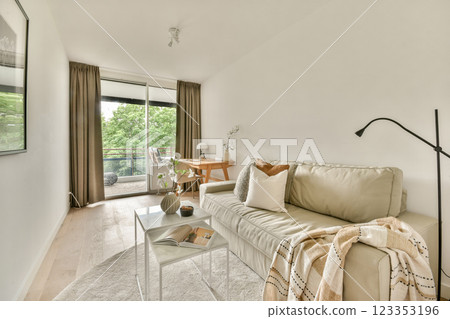 A stylish, modern living room showcasing minimalistic decor, featuring a cozy couch, wooden table, and large windows for natural light. 123353196