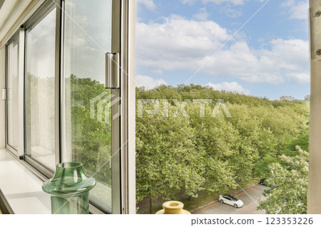 A serene view of lush greenery outside a large window, showcasing a peaceful urban landscape with trees and a hint of road. 123353226