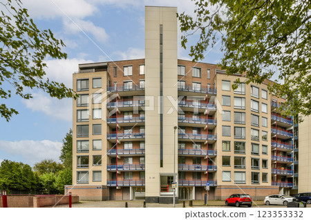 A contemporary residential complex featuring multiple balconies and a unique architectural design, surrounded by greenery and blue skies. 123353332