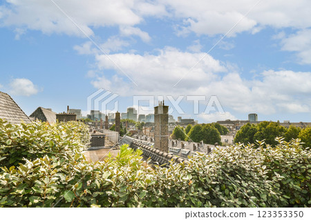 A panoramic view of the city skyline featuring modern buildings framed by lush greenery under a bright blue sky with fluffy clouds. 123353350