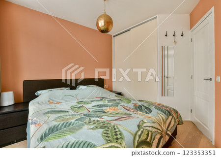 A modern bedroom featuring a cozy bed adorned with a leafy comforter, warm wall colors, and minimalist decor for a relaxing atmosphere. A modern bedroom featuring a cozy bed adorned with a leafy comforter, warm wall colors, and minimalist decor for a relaxing atmosphere. 123353351