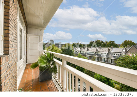A picturesque balcony adorned with greenery, offering a scenic view of the city skyline and neighboring houses bathed in natural light and blue skies. A picturesque balcony adorned with greenery, offering a scenic view of the city skyline and neighboring houses bathed in natural light and blue skies. 123353373