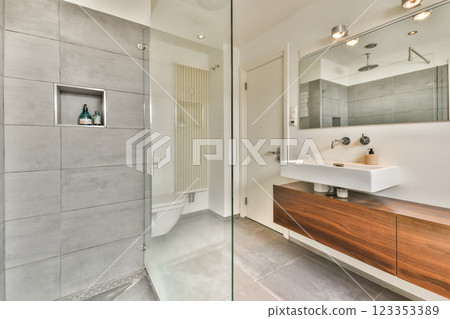 A contemporary bathroom featuring sleek gray tiles, a minimalist sink, and stylish wooden cabinetry, creating a fresh and elegant atmosphere. 123353389