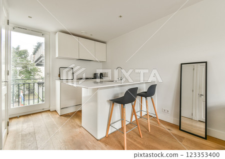 A stylish minimalist kitchen featuring sleek cabinetry and modern appliances, complemented by natural light and a clean aesthetic from the hardwood floor. 123353400