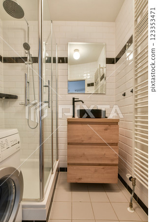 A sleek modern bathroom featuring a glass-enclosed shower, stylish fixtures, and wooden cabinetry against a minimalist tile backdrop. A sleek modern bathroom featuring a glass-enclosed shower, stylish fixtures, and wooden cabinetry against a minimalist tile backdrop. 123353471