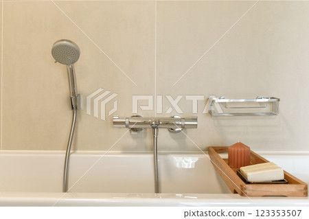A stylish bathroom featuring a mounted showerhead, sleek faucet, and a wooden tray displaying soap and decor items for a contemporary look. 123353507
