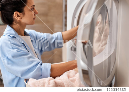 woman put pastel cotton towel in automatic washing machine at home woman put pastel cotton towel in automatic washing machine at home 123354885