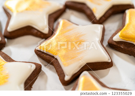 Close-up of a gingerbread star cookie painted with shimmering gold luster dust over smooth royal icing, highlighting the fine details. Close-up of a gingerbread star cookie painted with shimmering gold luster dust over smooth royal icing, highlighting the fine details. 123355029