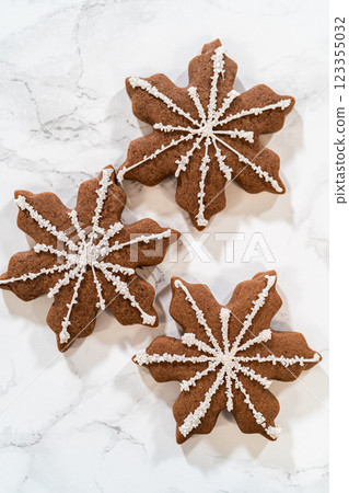 Top-down view of three chocolate ginger snowflake cookies, each beautifully decorated with royal icing and sugar crystals, arranged on a white marble surface for a festive display. Top-down view of three chocolate ginger snowflake cookies, each beautifully decorated with royal icing and sugar crystals, arranged on a white marble surface for a festive display. 123355032