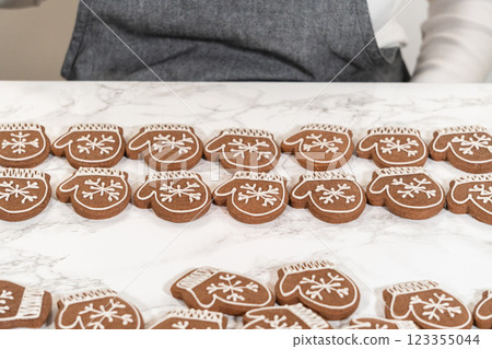 A final display of mitten-shaped gingerbread cookies fully decorated with intricate white icing patterns, arranged neatly on a marble surface. 123355044