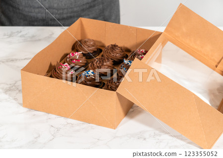 Preparing to share the delicious chocolate cupcakes, the final step involves carefully packaging them into a brown paper cupcake box. Preparing to share the delicious chocolate cupcakes, the final step involves carefully packaging them into a brown paper cupcake box. 123355052