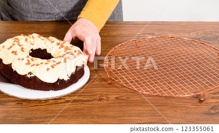 Carefully placing the gingerbread bundt cake, adorned with salted caramel frosting and gingerbread sprinkles, into a white paper bundt cake box with a clear window for gifting. 123355061