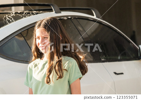 A young girl enthusiastically assists in washing the family's electric car in their suburban driveway. 123355071