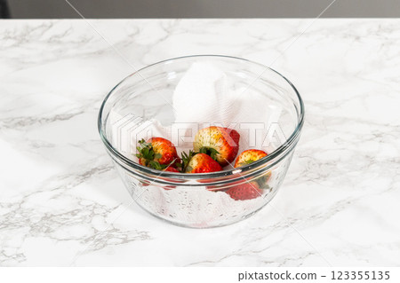 Freshly washed and dried strawberries are carefully arranged in a glass bowl lined with paper towel, ready for snacking or further use. 123355135