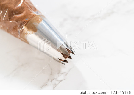The chocolate icing is carefully transferred into a piping bag, ready to adorn the scrumptious cupcakes. The chocolate icing is carefully transferred into a piping bag, ready to adorn the scrumptious cupcakes. 123355136