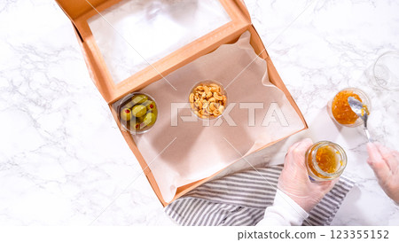 Flat lay. Hands are meticulously adding fresh red grapes to a bowl, complementing a beautifully arranged charcuterie box brimming with a variety of cheeses, olives, and cured meats, set against a Flat lay. Hands are meticulously adding fresh red grapes to a bowl, complementing a beautifully arranged charcuterie box brimming with a variety of cheeses, olives, and cured meats, set against a 123355152