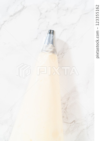 The creamy and delicious cream cheese buttercream frosting is artfully transferred to a piping bag, featuring a round metal piping tip, ready for decorating the Carrot Bundt Cake. 123355162
