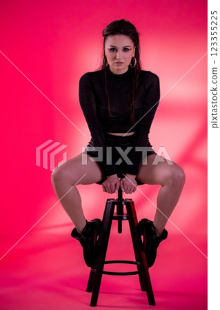 A Stylish Model Posing on a Stool Against a Vibrant Pink Background in a Studio Setting 123355225
