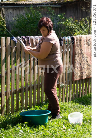A woman is hanging socks on a wooden fence in her backyard. She is doing laundry on a sunny day outdoors with green grass and trees. A woman is hanging socks on a wooden fence in her backyard. She is doing laundry on a sunny day outdoors with green grass and trees. 123356071