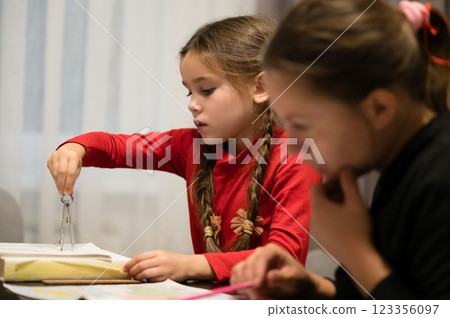 Focused young girl concentrating on math homework using a compass, her friend is besides her and appears deep in thought. Focused young girl concentrating on math homework using a compass, her friend is besides her and appears deep in thought. 123356097
