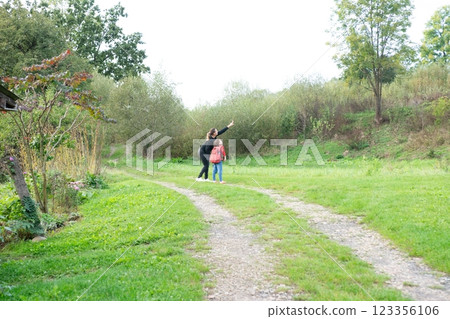 Mother and daughter on a country road enjoying nature, the mother is pointing to something interesting as they explore on a summer day. Mother and daughter on a country road enjoying nature, the mother is pointing to something interesting as they explore on a summer day. 123356106