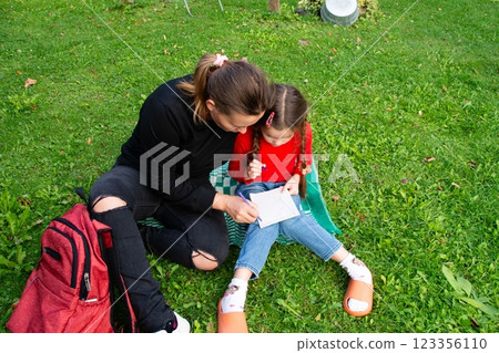 A mom and daughter bonding over a drawing outside on a green lawn, enjoying a sunny day and creating art together. 123356110