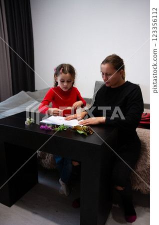 A girl and woman study flora together at a dark table with flowers and leaves. Family time while learning about nature. 123356112