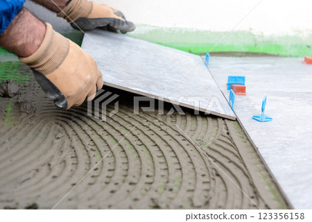 Tiler at work installing new floor with tiles. Construction. 123356158
