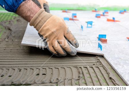 Tiler at work installing new floor with tiles. Construction. 123356159