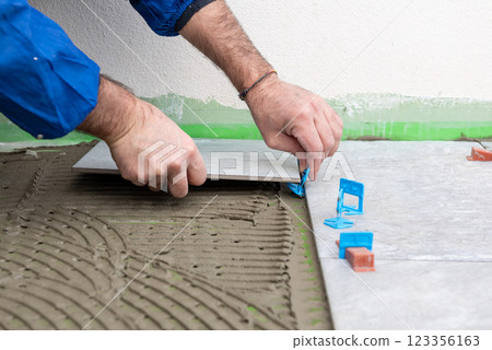 Tiler at work installing new floor with tiles. Construction. 123356163