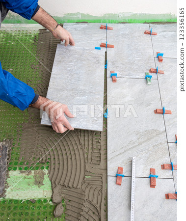 Tiler at work installing new floor with tiles. Construction. 123356165