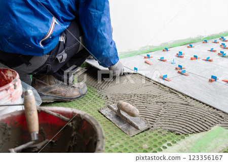 Tiler at work installing new floor with tiles. Construction. 123356167