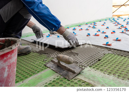 Tiler at work installing new floor with tiles. Construction. 123356170