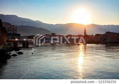 Sunset glows over a tranquil bay with the charming old town of Budva set against a backdrop of majestic mountains. 123356250