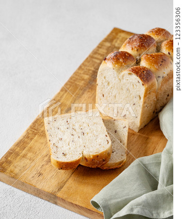 Freshly baked whole grain bread with slices on a wooden board with a napkin on a light background. Freshly baked whole grain bread with slices on a wooden board with a napkin on a light background. 123356306